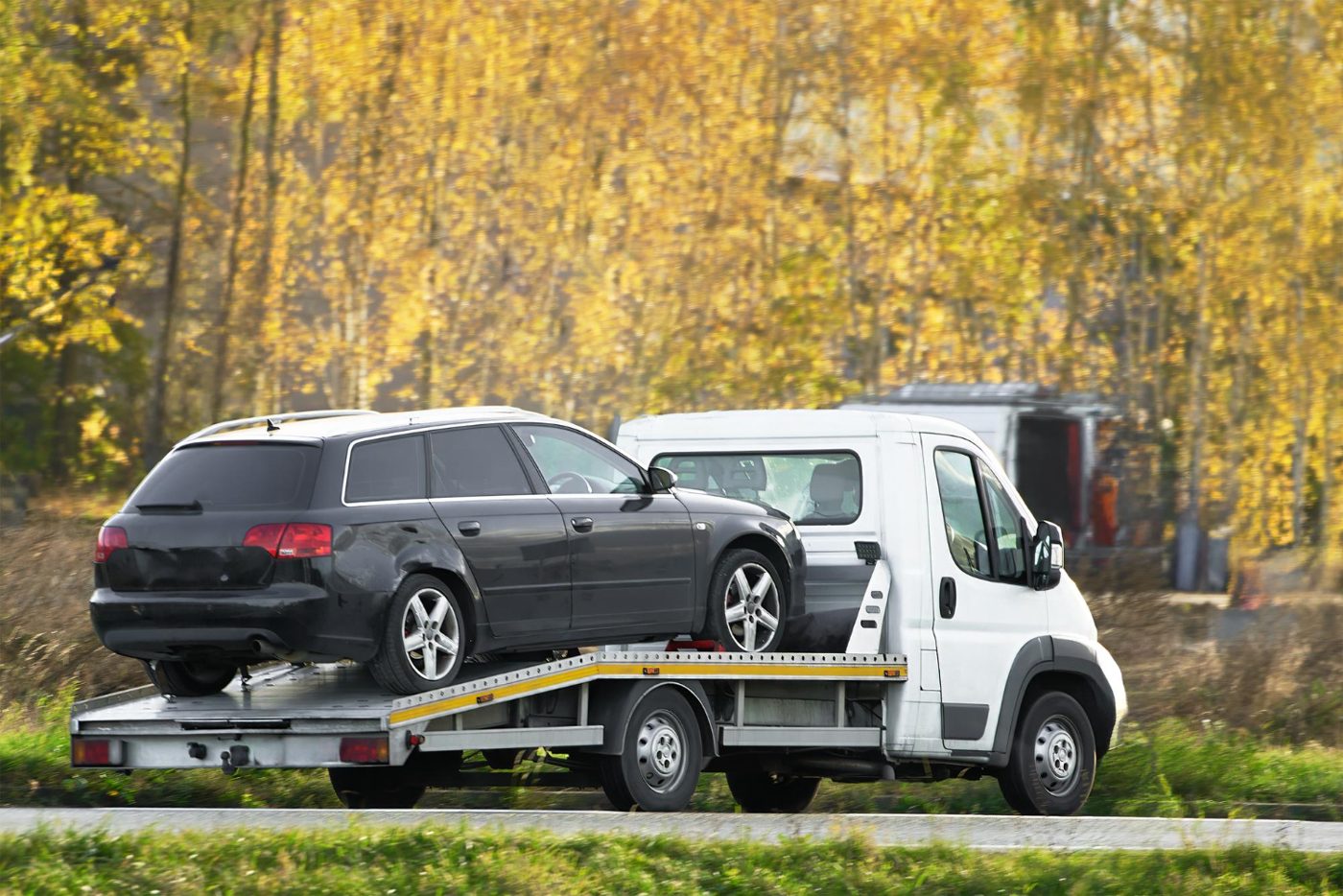 Carroattrezzi con station wagon nera in una strada alberata